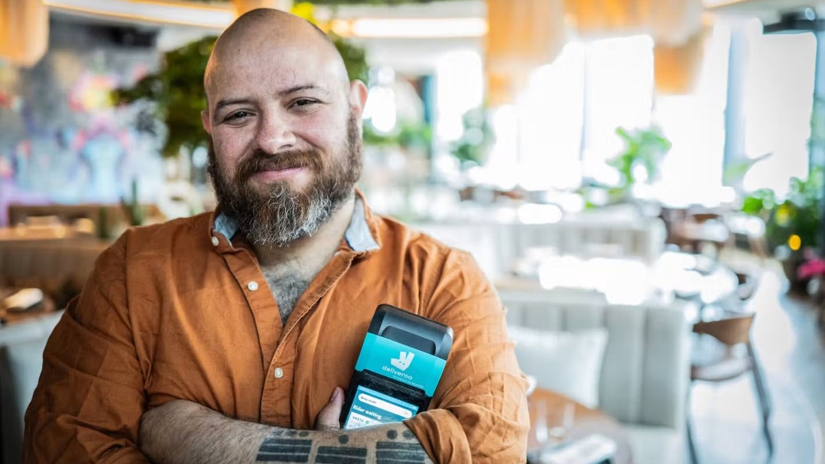 A restaurant owner holding a Deliveroo order tablet.