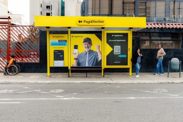 A yellow PagoEfectivo bus shelter advert showing the campaign ambassador holding a phone with the wallet app.